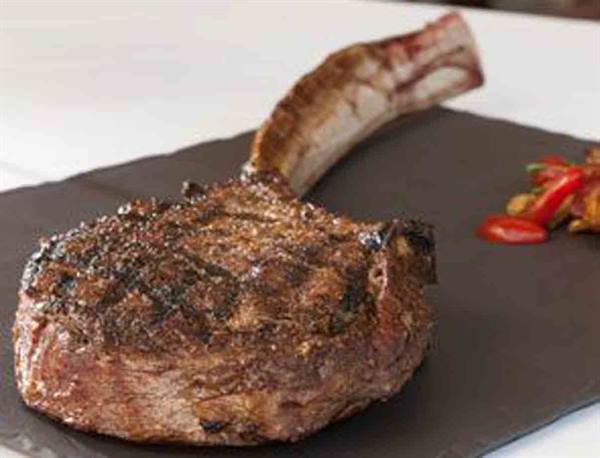 Grilled tomahawk steak on slate board with chili peppers beside