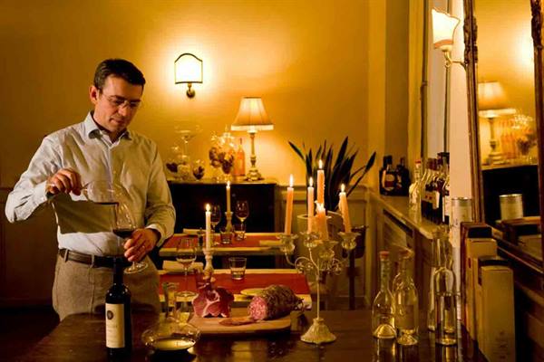 Waiter pouring wine beside cured meats, lit candles and glowing lamps