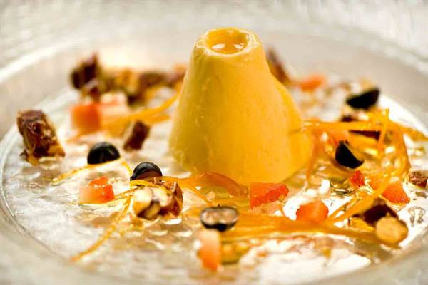 Yellow cone-shaped dessert on jelly with fruit and orange zest
