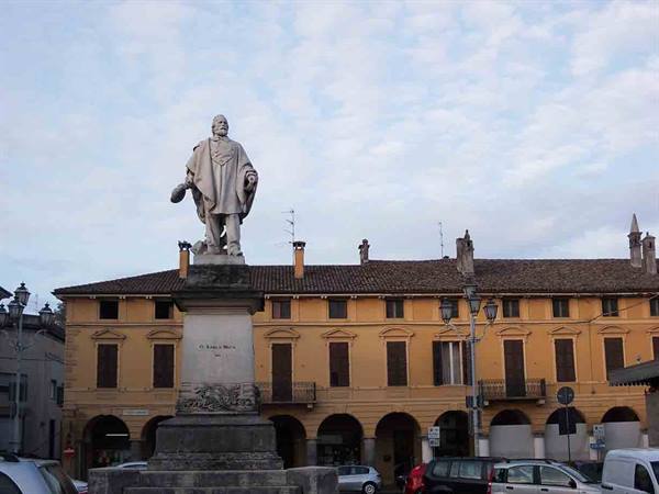 Marble statue on pedestal in front of yellow arcade building