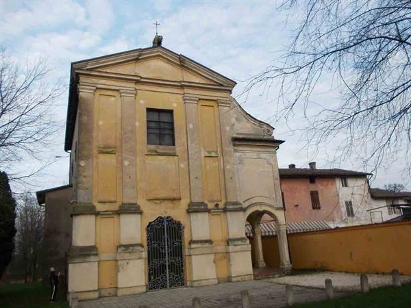 Ochre-yellow church with wrought iron gate under cloudy sky