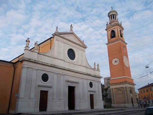 White church facade with statues and brick bell tower under cloudy sky