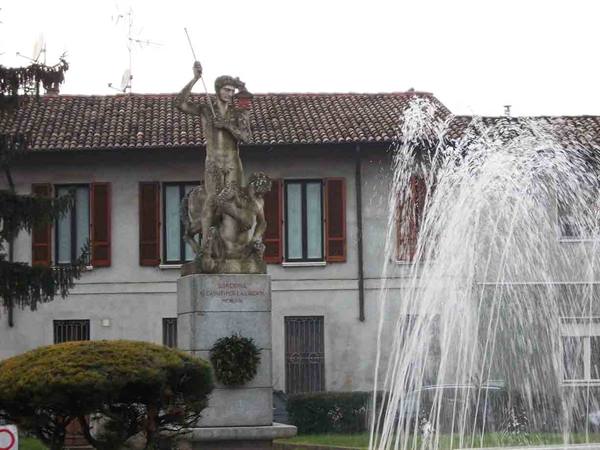 Stone statue on pedestal before tiled-roof building, water jets spraying
