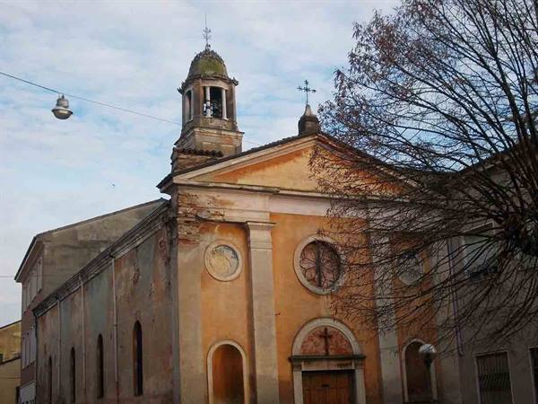 Ochre plastered church with green domed bell tower, bare branches in foreground