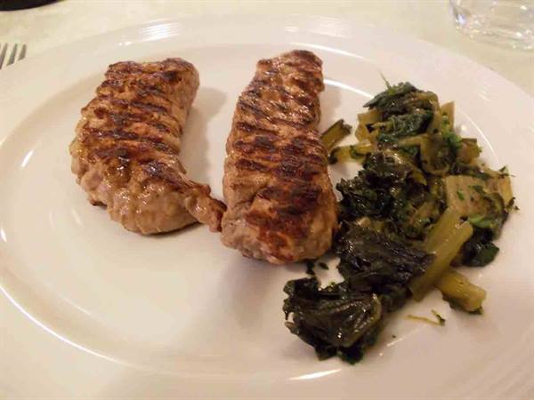 Two grilled sausages with sautéed greens on a white plate