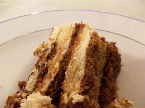 Slice of tiramisu with cream and ladyfinger layers, on a white plate