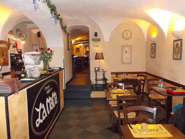 Trattoria dining room with white vaulted ceilings, wooden counter, set tables and warm lighting
