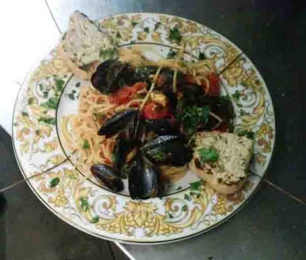 Spaghetti with mussels, cherry tomatoes and toasted bread on ornate golden plate
