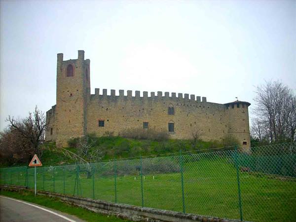 Stone medieval fortress with battlements and tower, green fence and meadow below