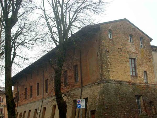 Old ochre brick building among bare trees under grey winter sky