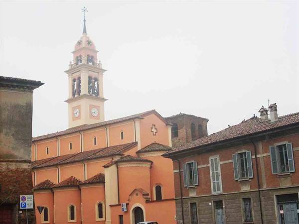 Salmon-colored church with bell tower and clock among houses under gray sky