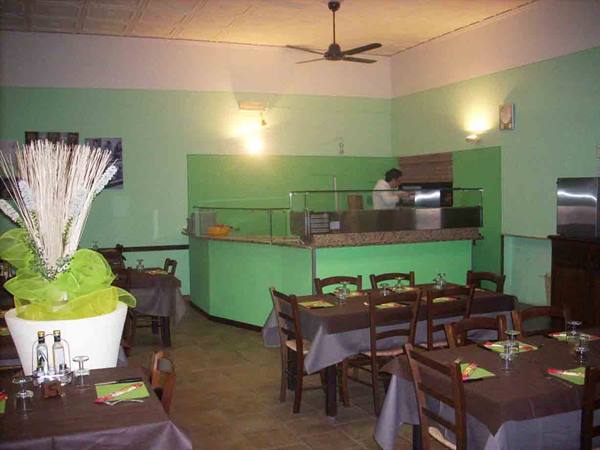 Pizzeria dining room with set tables, green counter and pizza chef at work