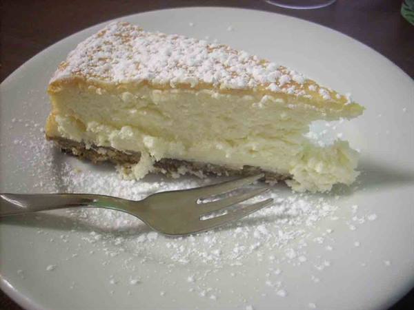 Cheesecake slice with powdered sugar on white plate, silver fork