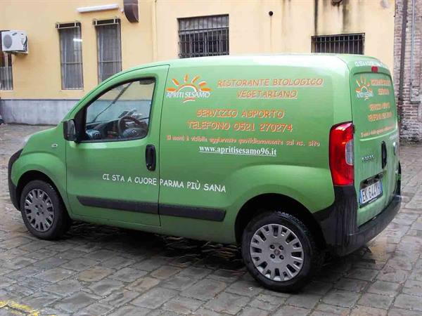 Green delivery van for vegetarian restaurant Apriti Sesamo, orange lettering, parked on cobblestones
