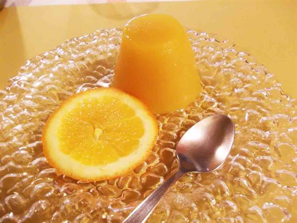 Orange jelly on textured glass plate with orange half and spoon