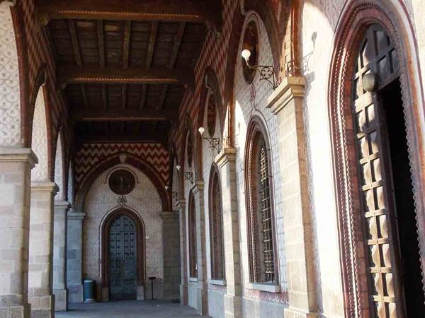 Brick and stone arcaded loggia with arched wooden doors in warm sunlight