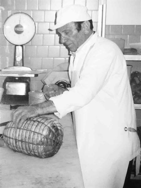 Butcher in white coat ties a netted porchetta on the counter