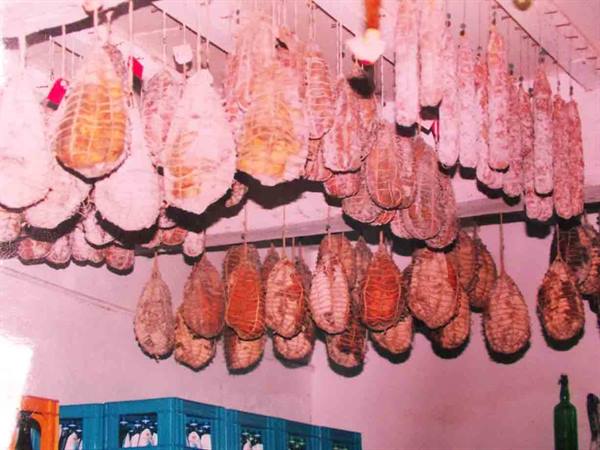 Aged cured meats hanging from ropes in a cellar, white walls, warm light