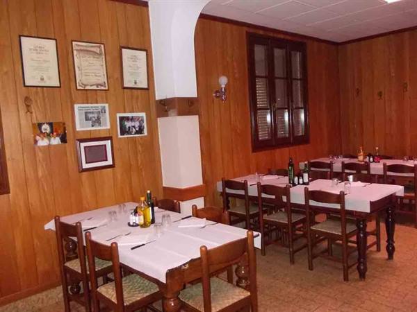 Wood-paneled trattoria dining room with set tables and framed certificates on walls