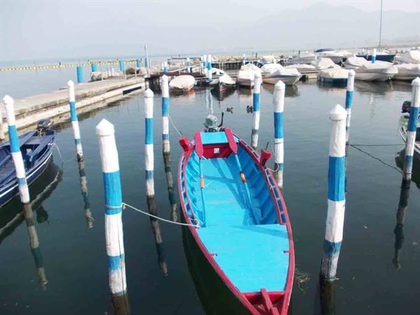 Blue and red boat moored between white and blue poles in the harbor