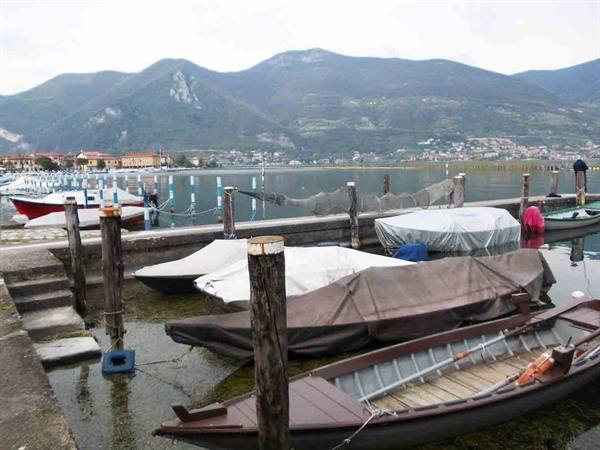 Wooden covered boats moored at posts, Lake Iseo with mountains behind
