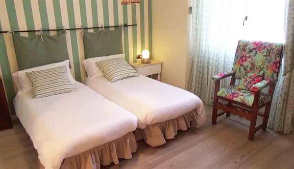 Twin bedroom with white beds, green striped wall and floral wooden armchair
