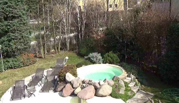 Round green pool among boulders, brown loungers and bare trees in the garden
