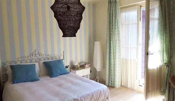 Bedroom with white wrought iron bed, turquoise pillows, black woven lamp, green curtains