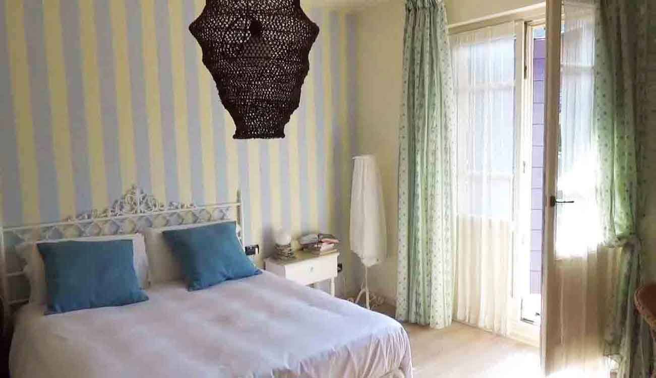 Camera da letto con letto a ferro battuto bianco, cuscini turchesi, lampadario nero, tende verdi