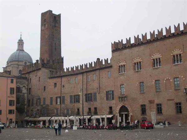 Mantua, Piazza Sordello: crenellated brick palace, tower and dome under grey sky