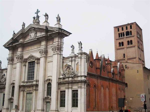 Baroque facade of Mantua Cathedral with marble statues and brick bell tower under grey sky