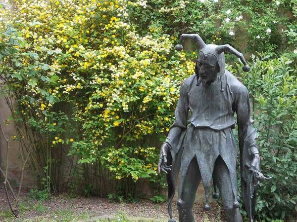 Bronze statue of a medieval jester among yellow flowering bushes