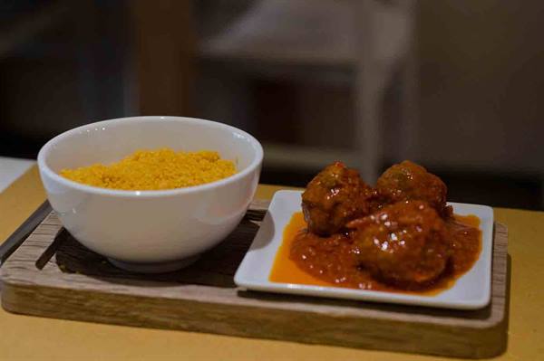 Bowl of couscous and meatballs in tomato sauce on wooden board