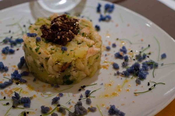 Seafood salad topped with black flakes, plated on white dish with blue edible flowers