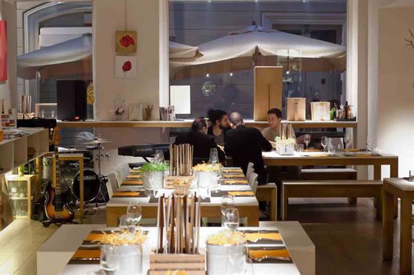 Dining tables set with wooden centerpieces in a restaurant, people chatting near guitar and drums