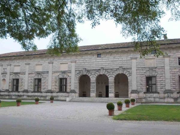 Stone facade with three arches, potted boxwoods, grey light, branches above