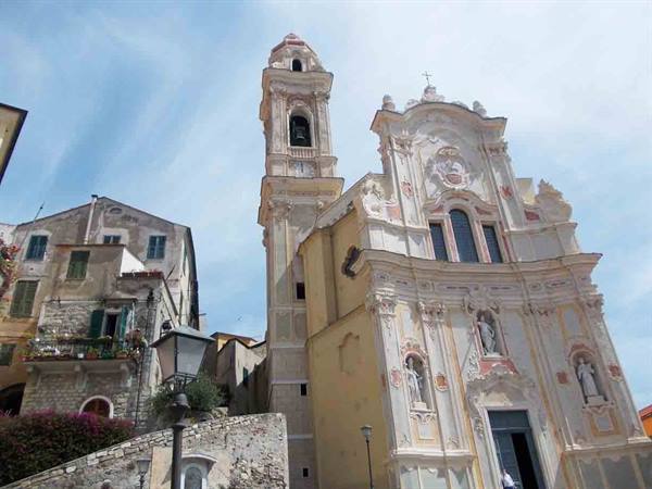 White baroque church with bell tower beside old stone houses, blue sky