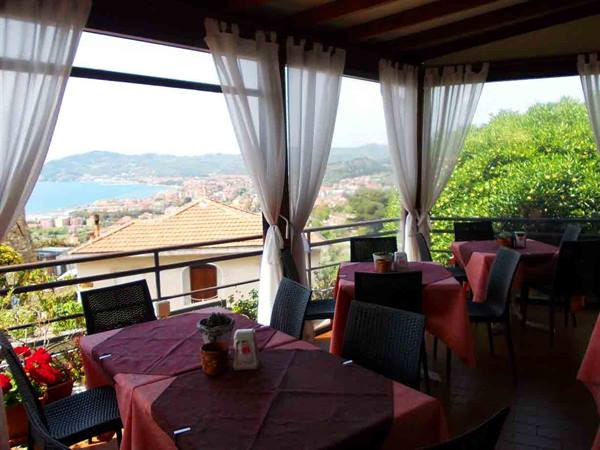 Restaurant veranda with set tables and white curtains overlooking a bay and rooftops