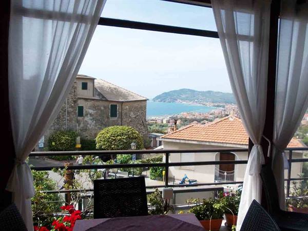 Veranda table with white curtains, stone houses and blue bay beyond