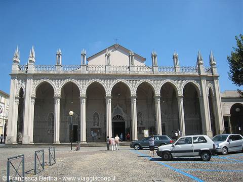 White facade of Biella Cathedral with arches and spires under blue sky