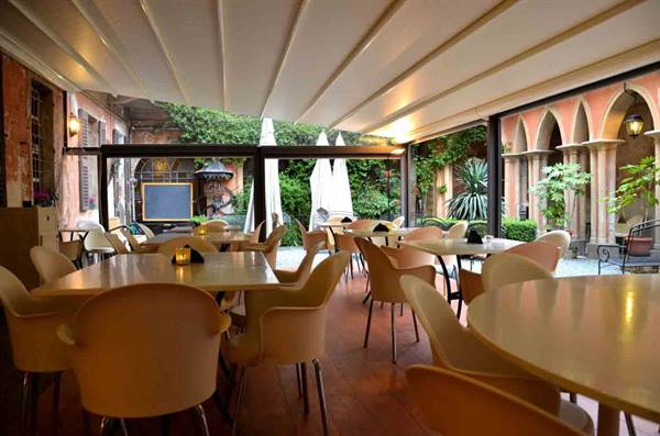 Empty tables under white canopy in cloister with arches and greenery