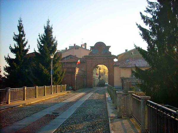 Brick gateway at the end of a cobblestone bridge, tall firs, morning light