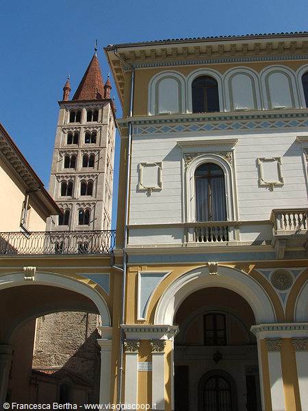Romanesque brick bell tower behind a yellow arcaded building under blue sky