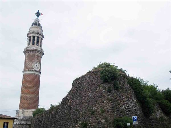 Brick bell tower with clock and statue beside old stone ruins