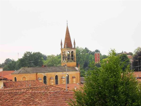 Yellow bell tower with spire among terracotta rooftops and green trees, grey sky