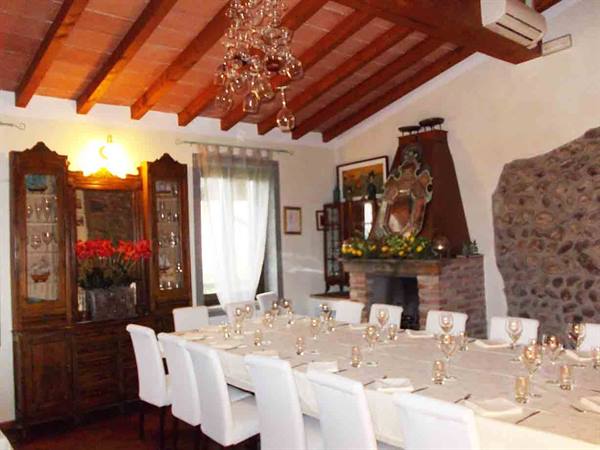 Set dining room with long table, white chairs, wooden ceiling and brick fireplace