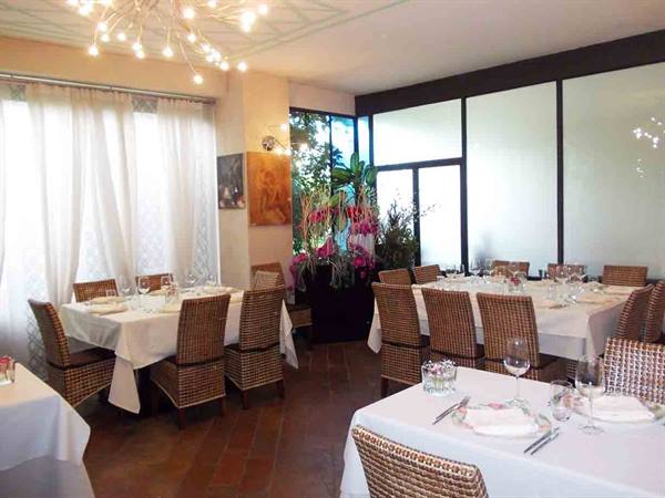 Restaurant dining room with white-tablecloth tables, wicker chairs and modern chandeliers