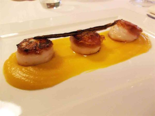 Seared scallops on pumpkin cream, white plate in a restaurant