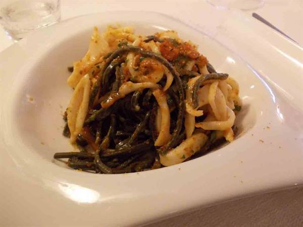 White plate with squid ink pasta and calamari, warm lighting