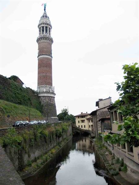Brick civic tower on green hill, Scarpatetti canal flowing between old houses in Busto Arsizio